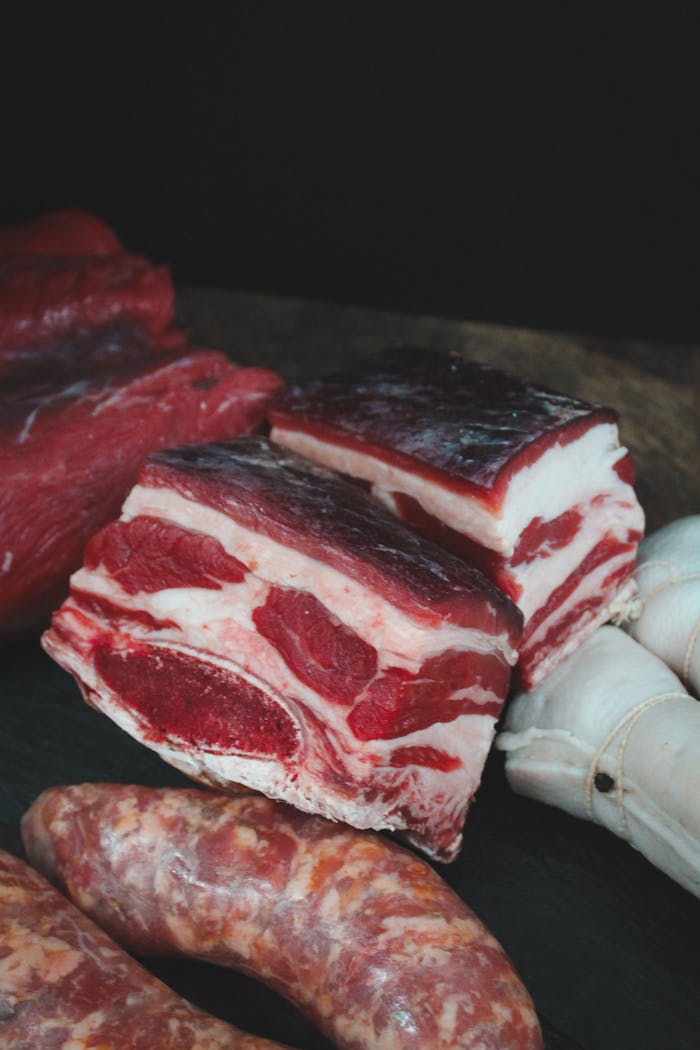 A diverse selection of raw meats including ribs and sausages on a dark surface.