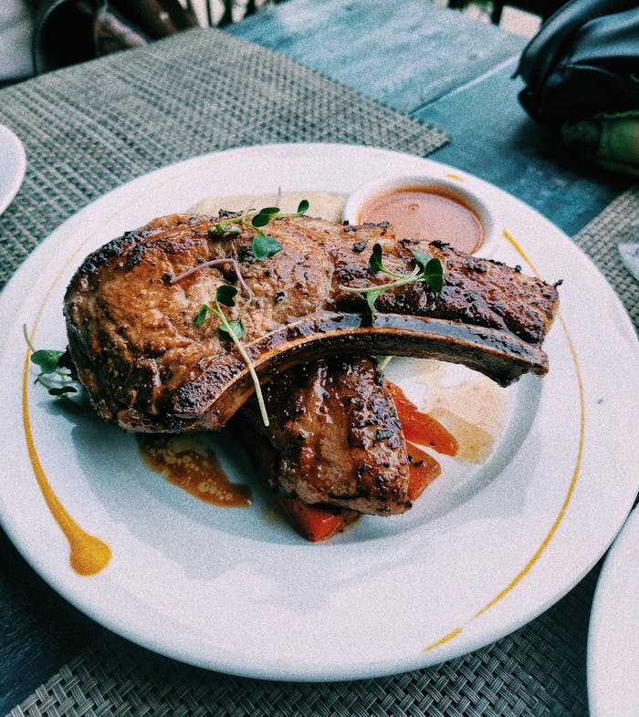 Delicious grilled pork chop served with sauce and herbs on a white plate. Perfect meal setting.