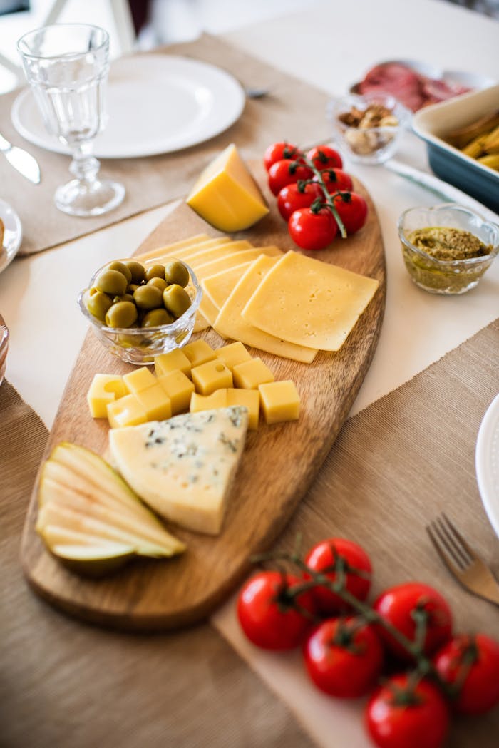 A gourmet cheese platter featuring assorted cheeses, olives, and fresh tomatoes, ideal for dining and food photography.