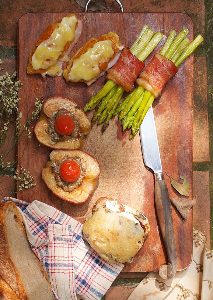 Tasty gourmet snacks including asparagus, cheese toast, and stuffed peppers on a wood board.